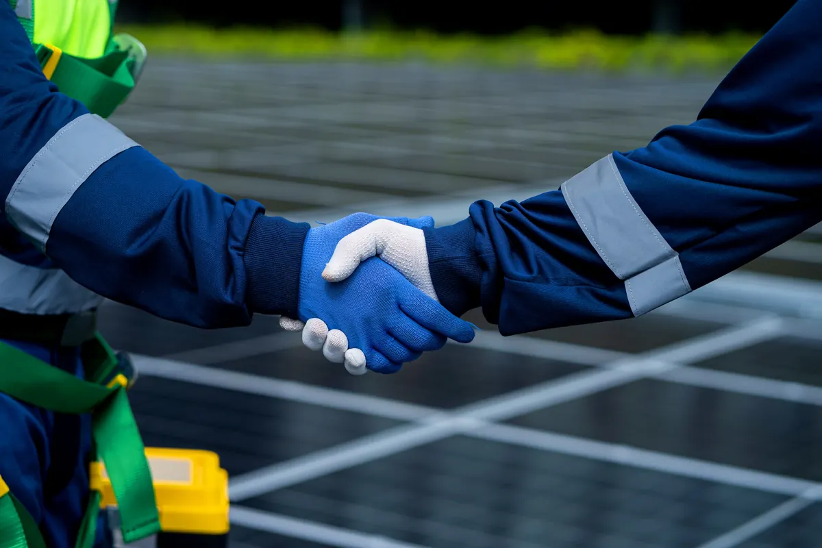Stretta di mano tra due tecnici davanti a un impianto fotovoltaico
